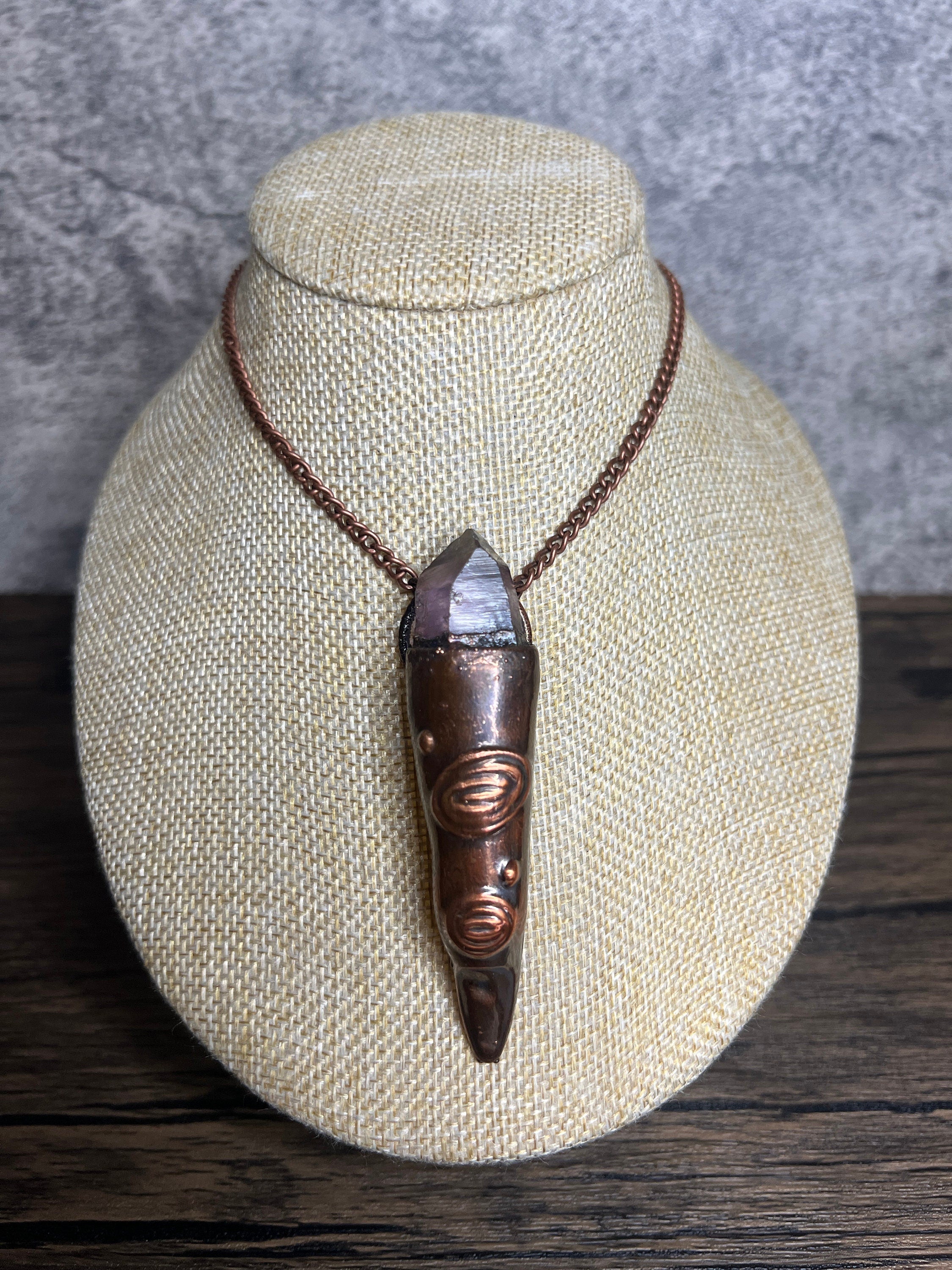 May include: A copper pendant necklace with a clear crystal point encased in a copper setting. The pendant is shaped like a long, pointed tooth with intricate details.