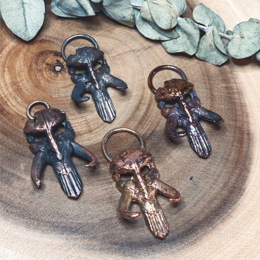 May include: Four metal pendants in the shape of a skull with horns. The pendants are in different shades of copper and bronze.