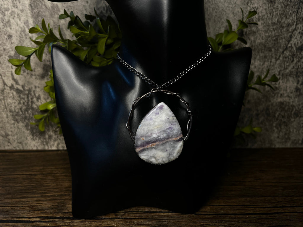 May include: A silver chain necklace with a teardrop-shaped pendant made of white and purple agate. The pendant is set in a silver wire frame.