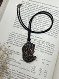 May include: A black cord necklace with a bronze pendant featuring a detailed depiction of Medusa, the Greek mythological figure with snakes for hair. The pendant is surrounded by text about electroplating and electroforming.
