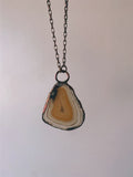 May include: A copper chain necklace with a pendant made from a slice of agate. The agate is a light brown color with white and gray banding.
