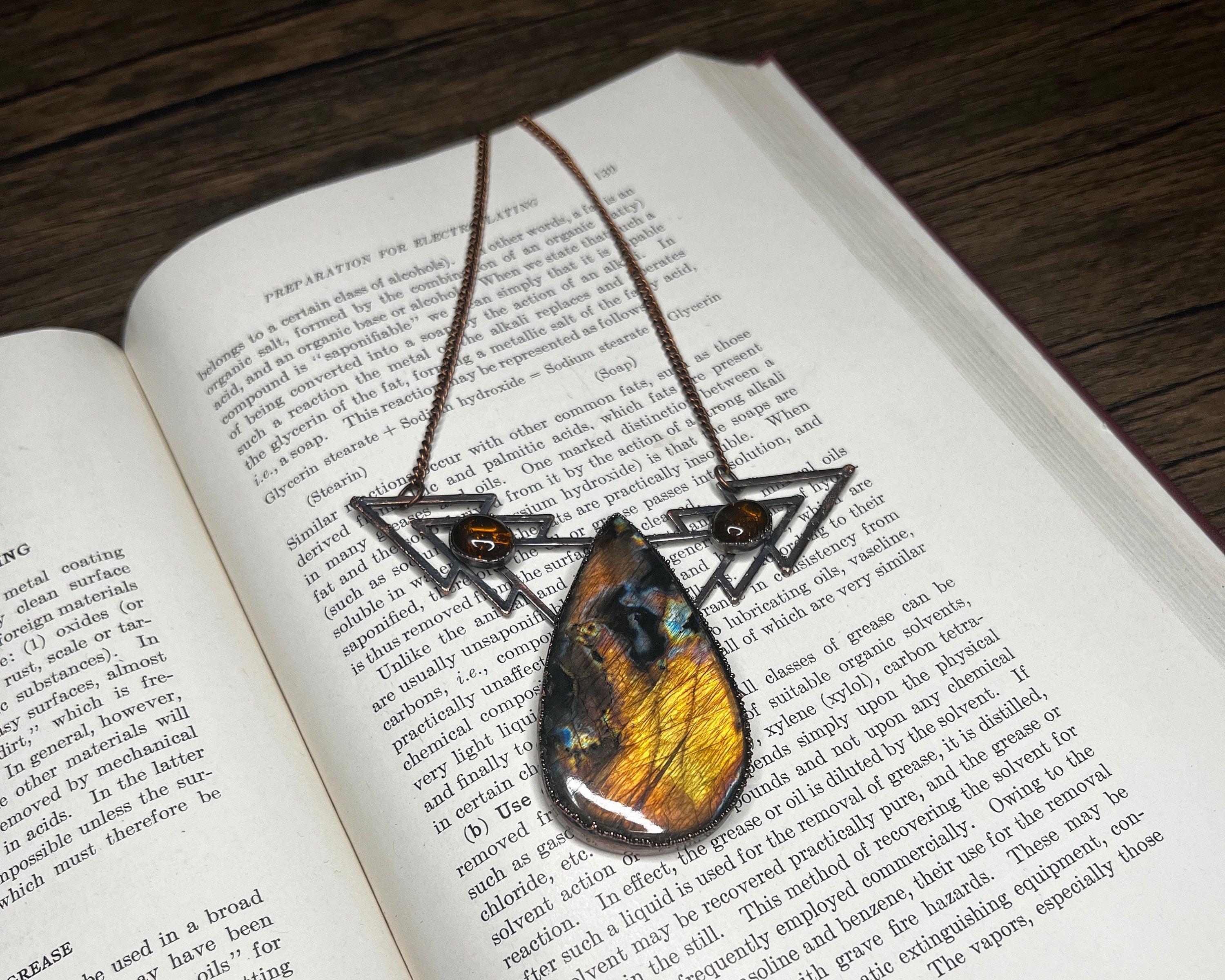 May include: A necklace with a teardrop-shaped pendant featuring a colorful butterfly wing encased in resin. The pendant is suspended from a metal chain with two triangular charms, each adorned with a brown gemstone.