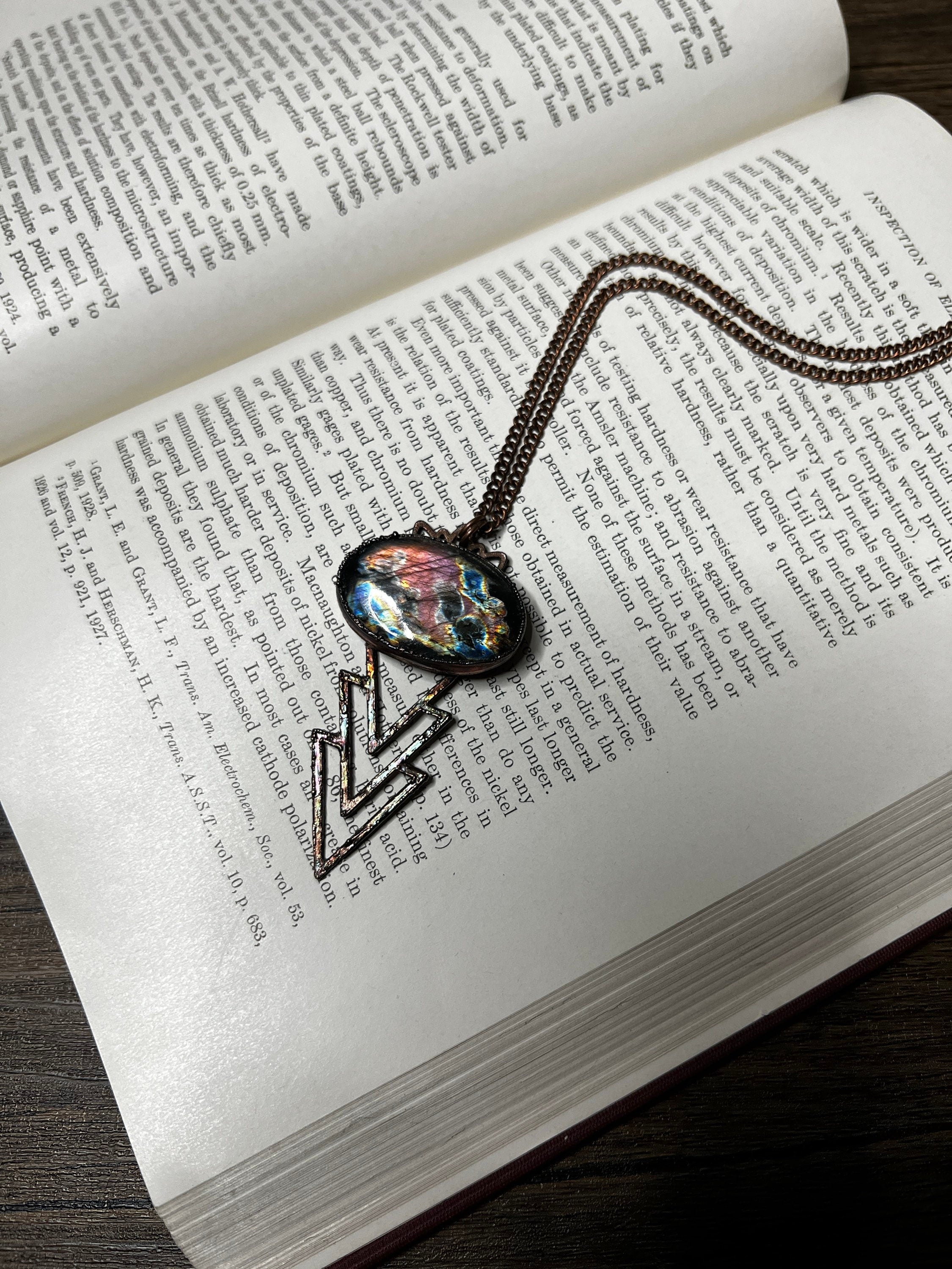 May include: A necklace with a bronze chain and a pendant featuring a triangular design with a blue, green, and purple iridescent glass inlay.