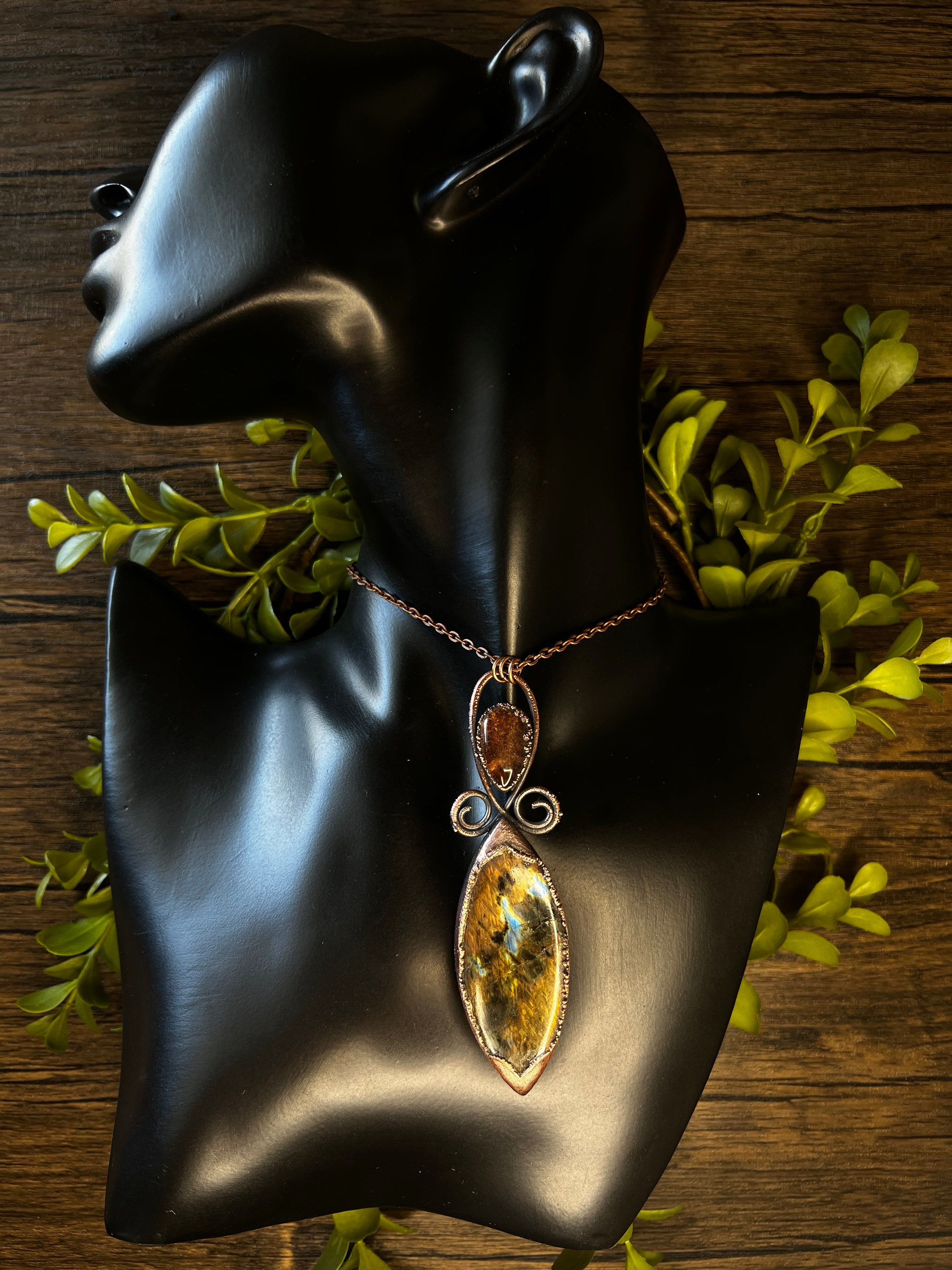 May include: A copper wire wrapped pendant necklace featuring a large, teardrop-shaped, iridescent gemstone with brown, gold, and green hues. The pendant is accented with a smaller, round, brown gemstone.