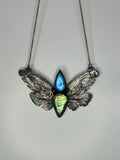 May include: A copper butterfly pendant necklace with a blue and green labradorite gemstone. The wings of the butterfly are detailed with intricate designs.