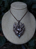 May include: A copper-toned pendant necklace featuring two jackalopes with prominent antlers, surrounded by intricate filigree leaf detailing and a small, iridescent blue cabochon stone at the base, suspended from a matching copper-colored chain.